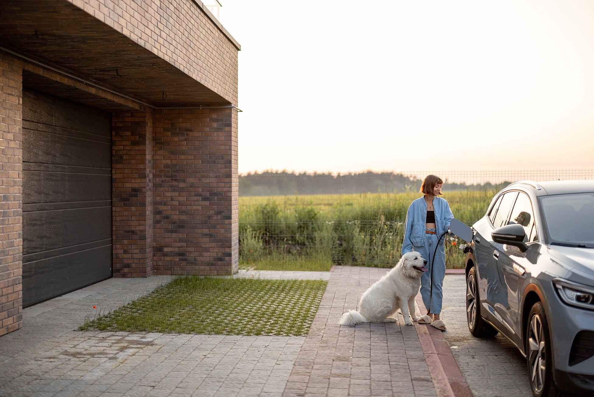 Junge Frau mit Hund lädt ein Elektroauto vor dem Haus