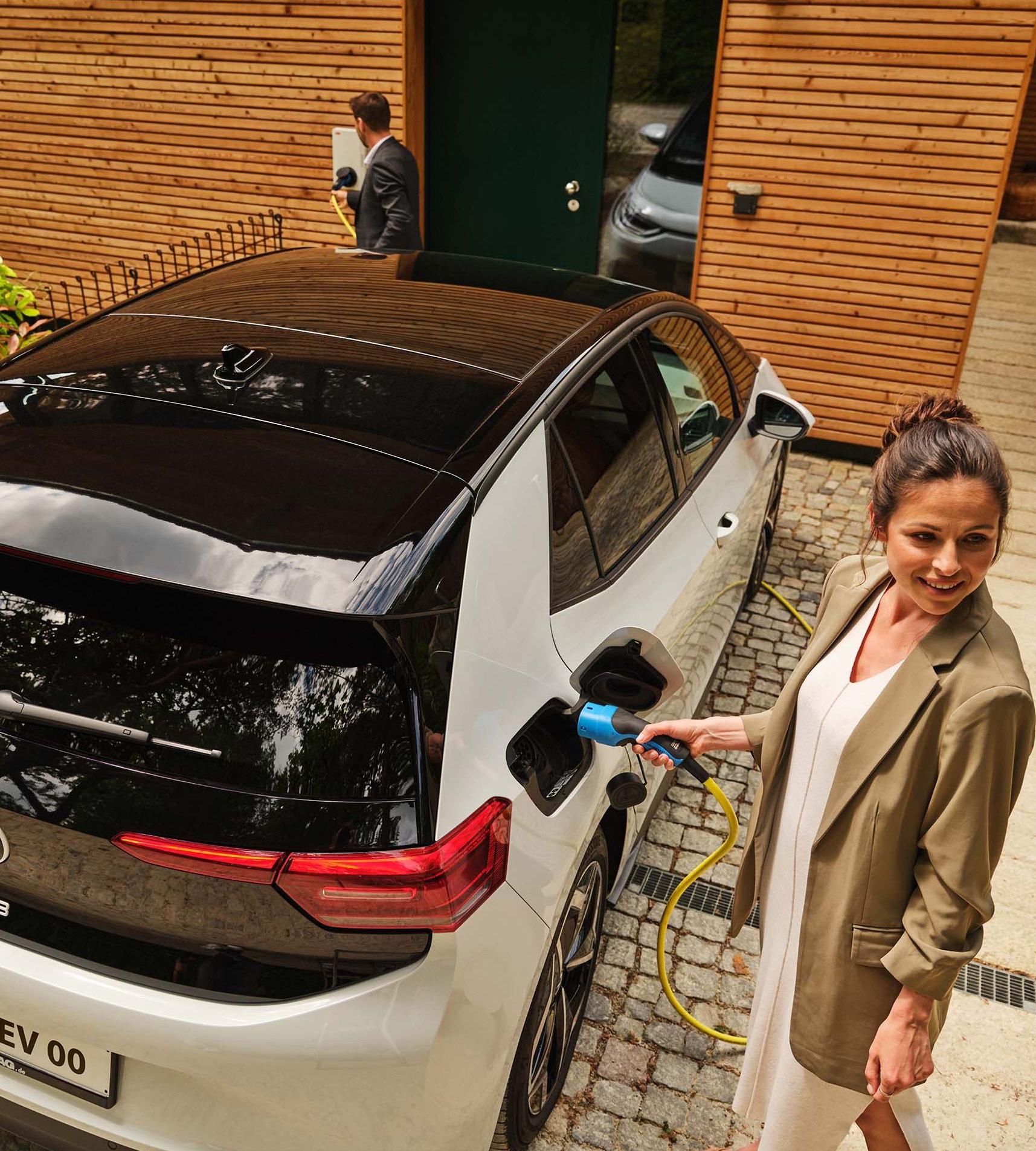 Frau lädt E-Auto vor Haus