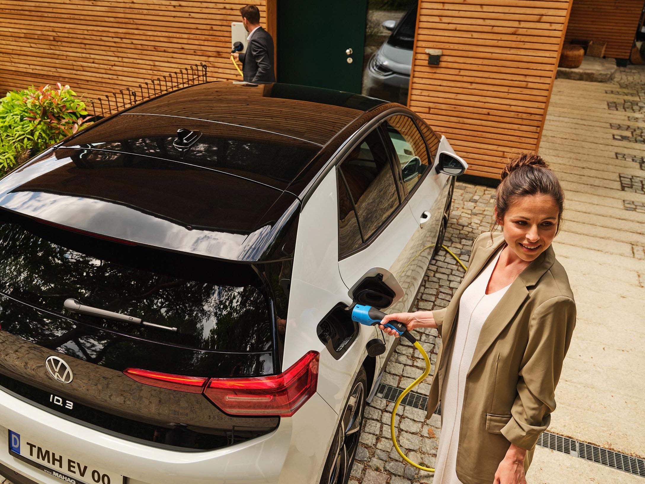 Frau lädt E-Auto vor Haus